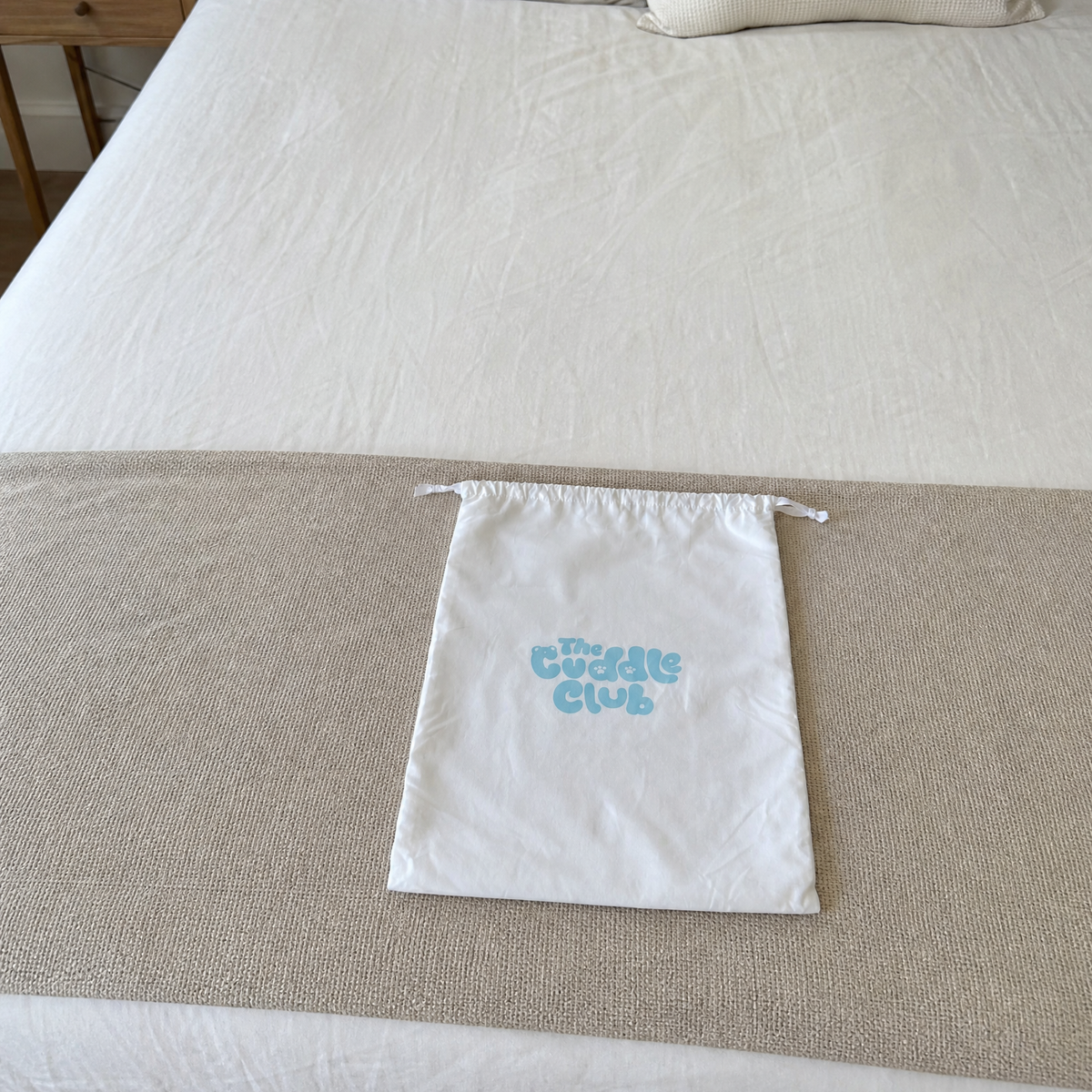 The Cuddle Club signature dust bag on a bed