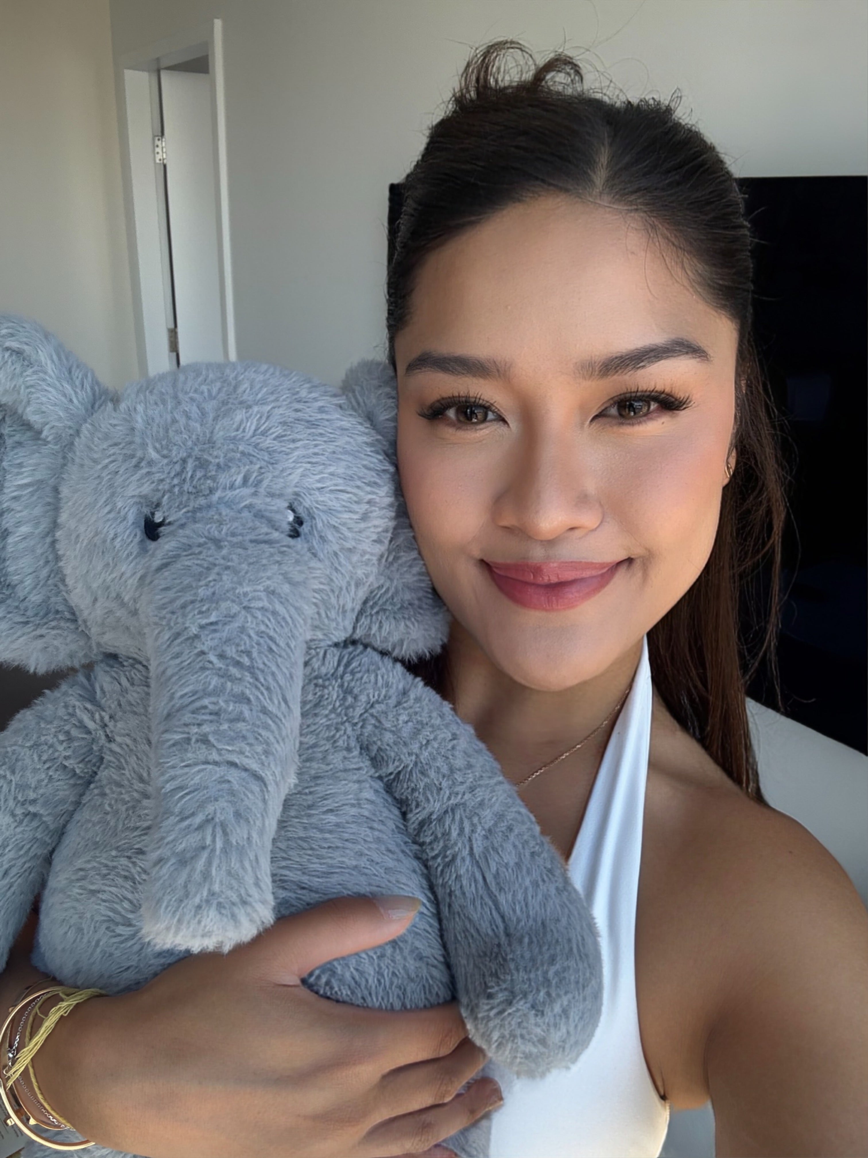 A woman holding a large gray plush elephant toy in a close-up selfie indoors.